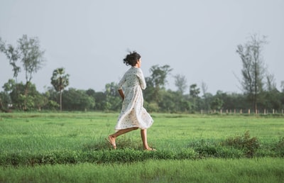 女人在白色礼服走在绿色草地白天
